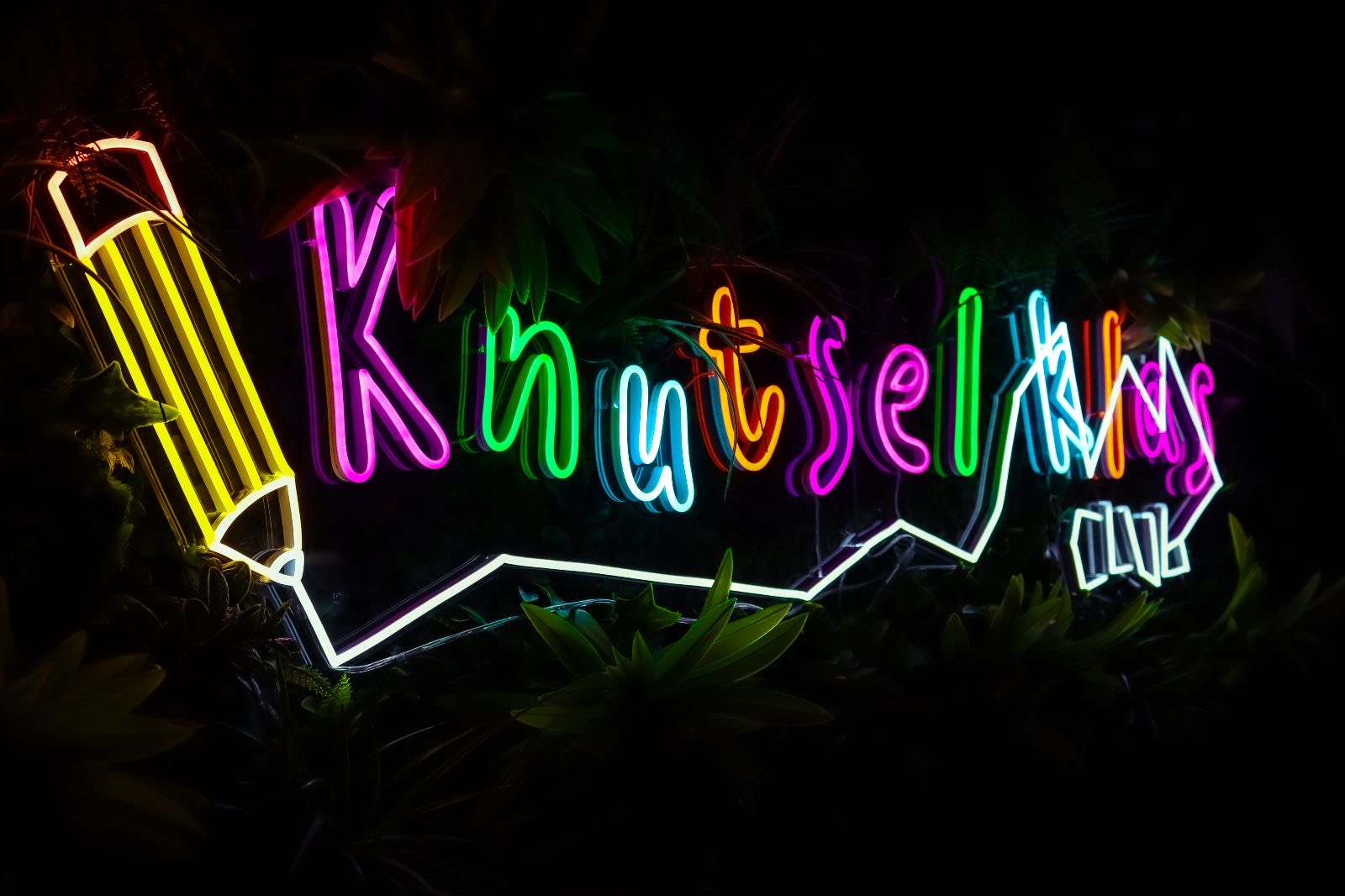 Mehrfarbiges Neon-Logo mit Bleistift-Symbol vor dunklem Hintergrund