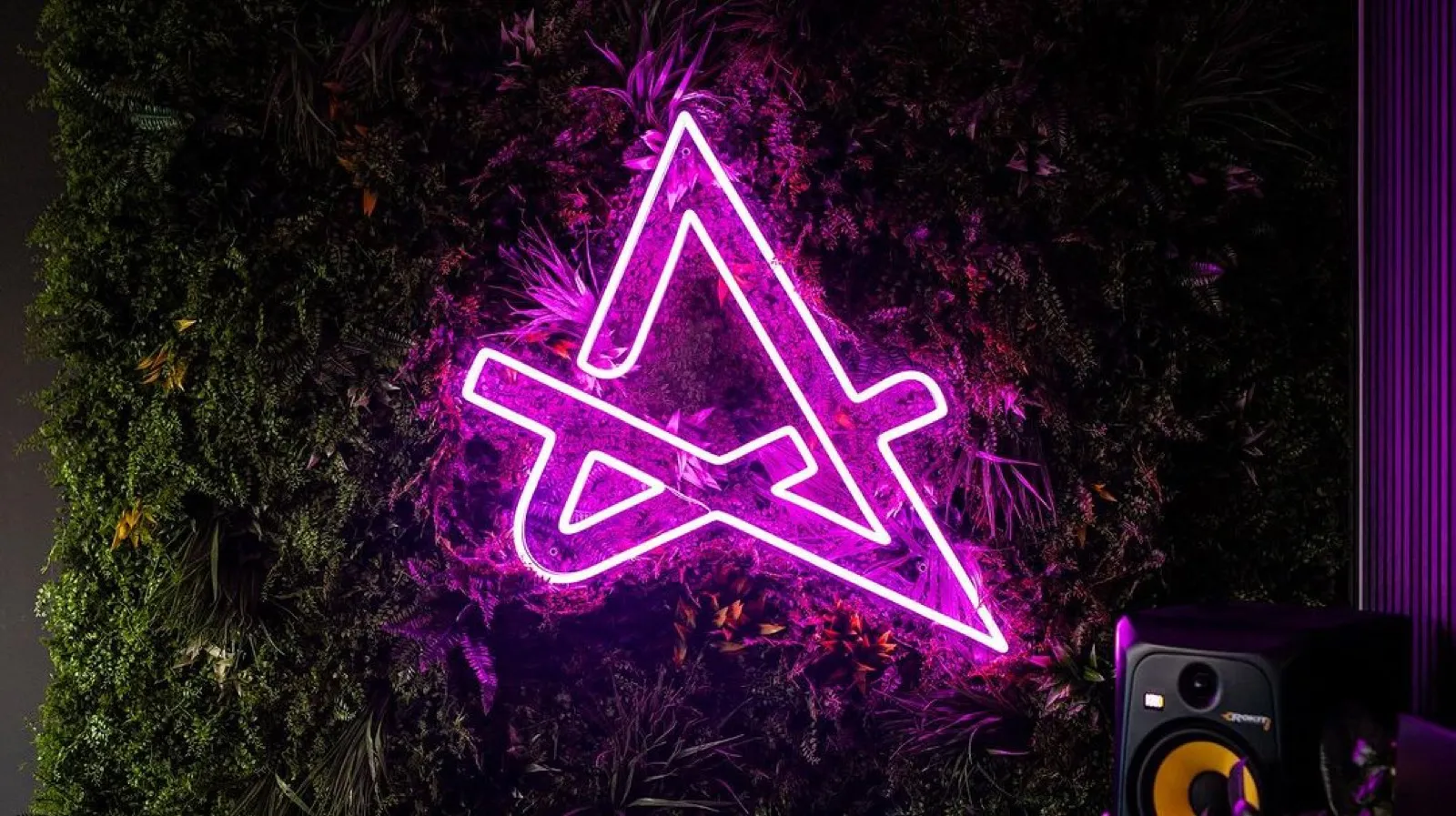 Gelbes Neon-Logo in Form eines Buchstaben R auf einer Mooswand im Büro